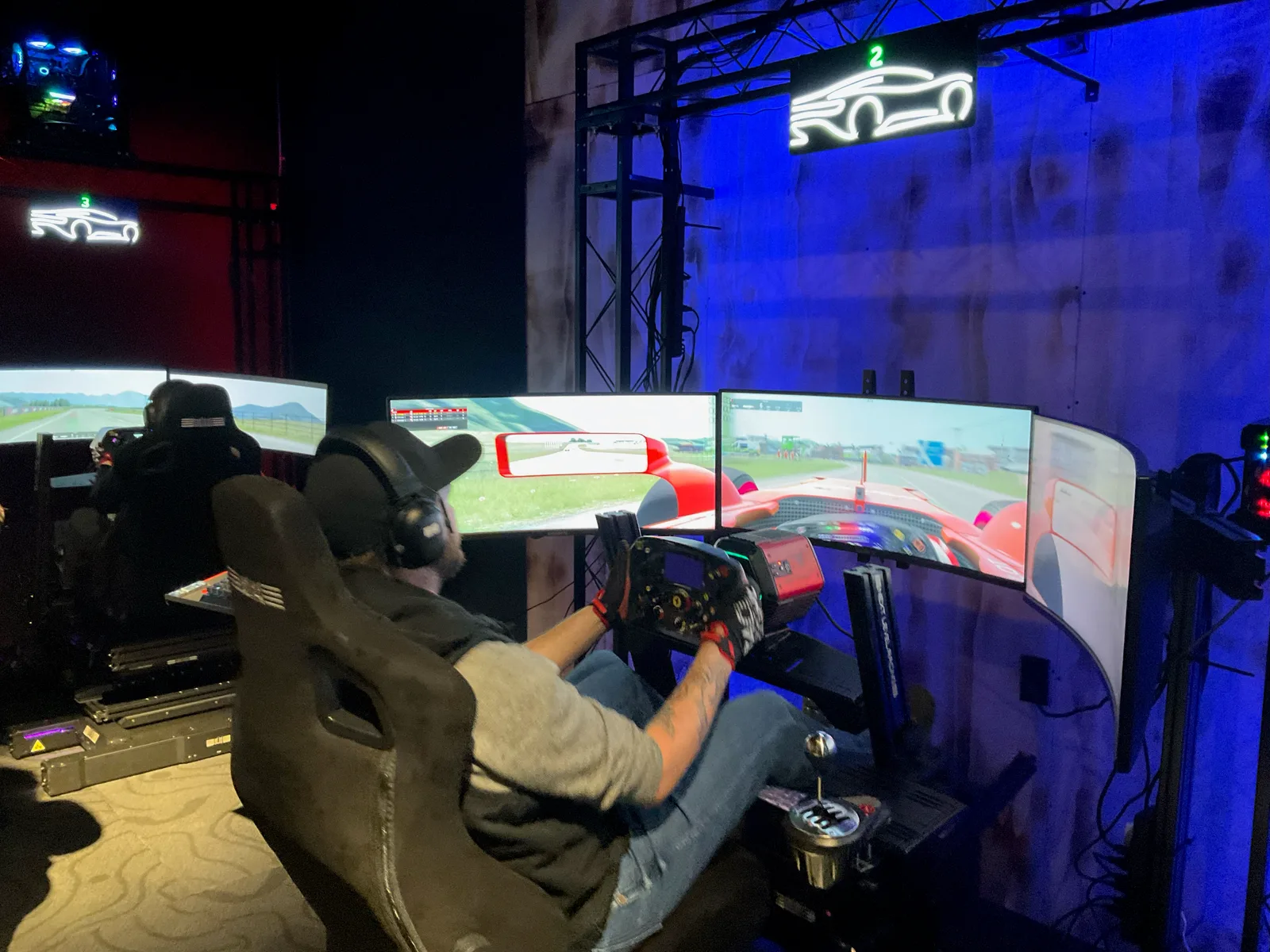 Driver using a triple-monitor racing cockpit in the blue-lit Simplex RaceZone.